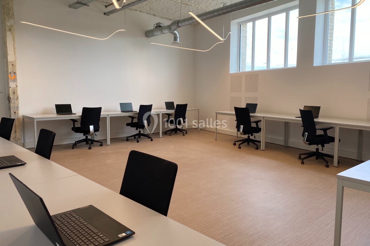 Salle de travail lumineuse avec plusieurs bureaux équipés de chaises et d'ordinateurs portables.