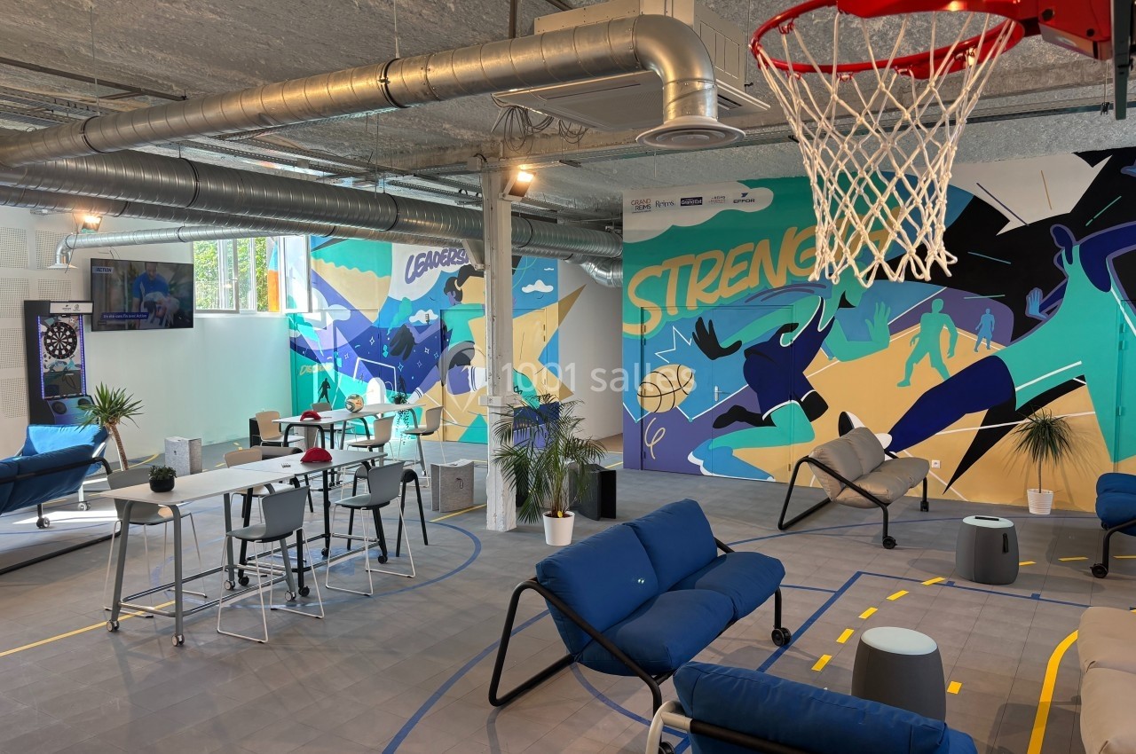 Espace de détente moderne avec canapés, tables, panier de basket et fresques murales colorées.