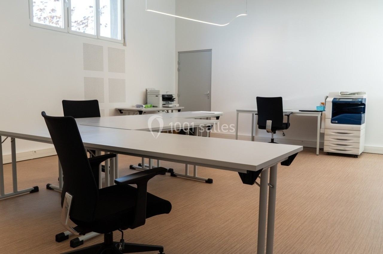 Bureau lumineux avec plusieurs postes de travail, chaises noires, imprimante et mobilier minimaliste.