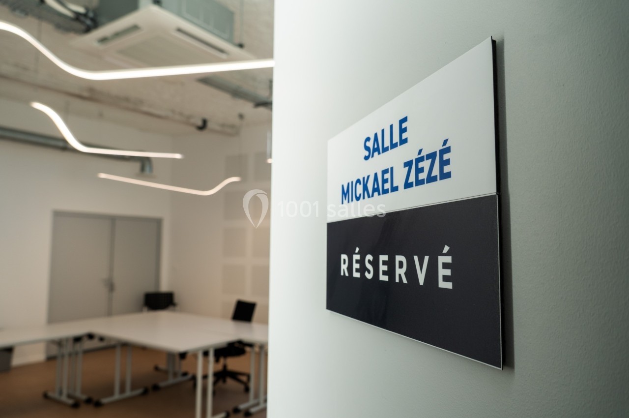 Panneau indiquant ’Salle Mickael Zézé - Réservé’ devant une salle de réunion moderne et vide.