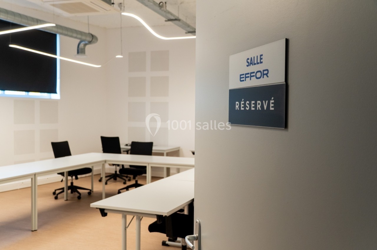 Salle de réunion moderne avec tables blanches, chaises noires et un panneau indiquant ’Réservé’ sur la porte.