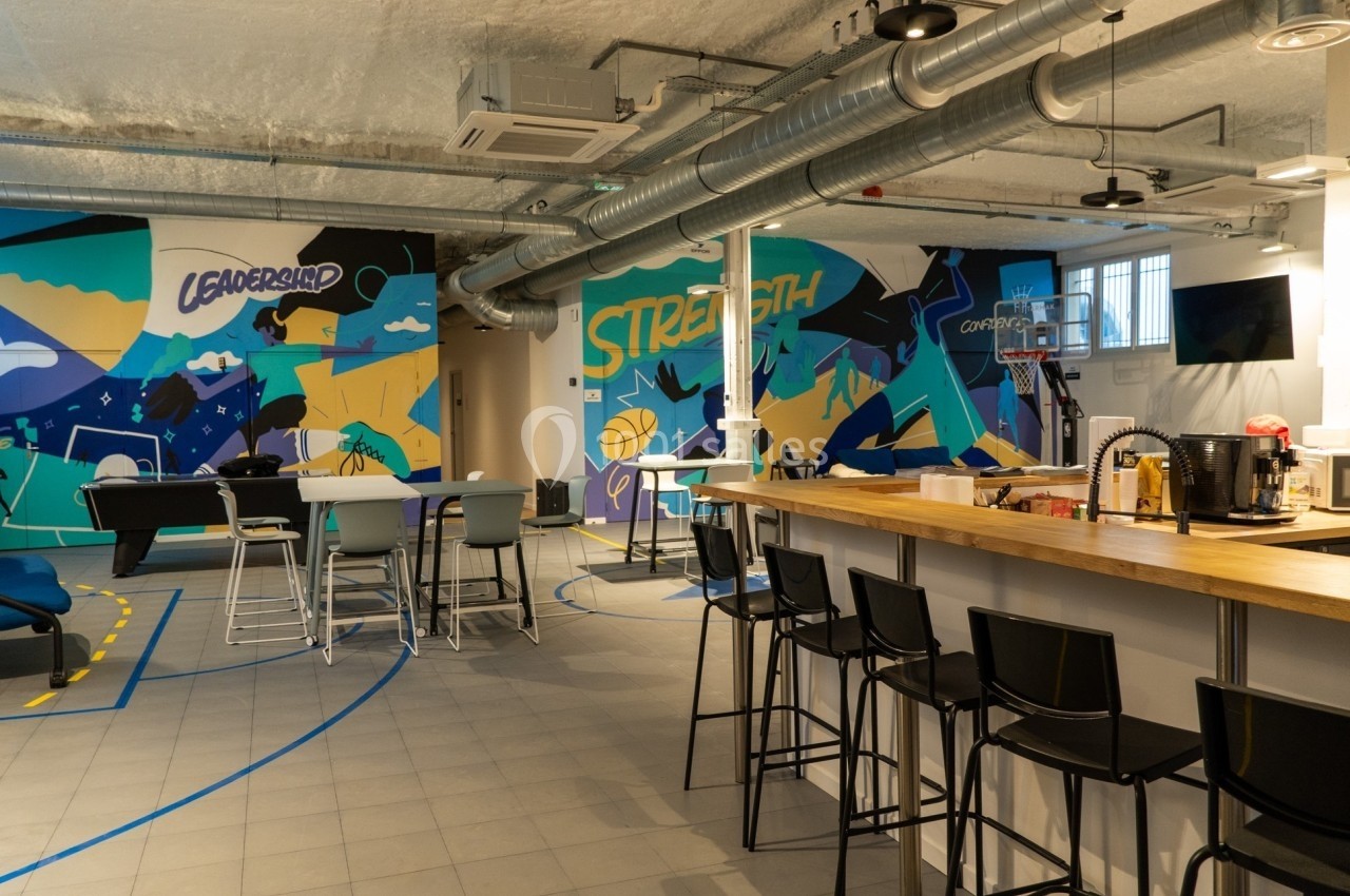 Espace intérieur moderne avec tables, chaises hautes, muraux colorés et un panier de basketball.