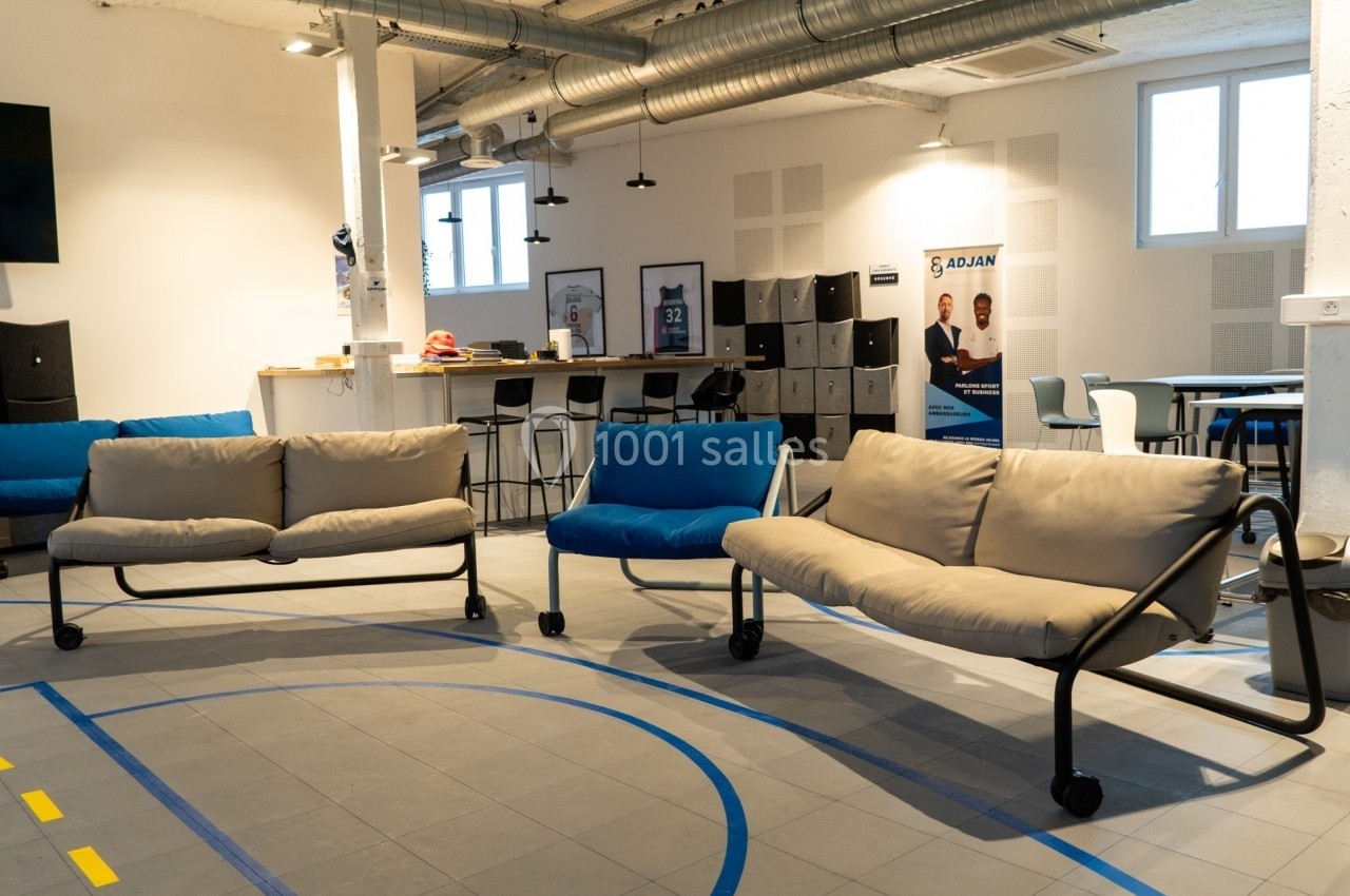 Espace intérieur lumineux avec canapés modernes, tables hautes, casiers et affiches dans un cadre professionnel.