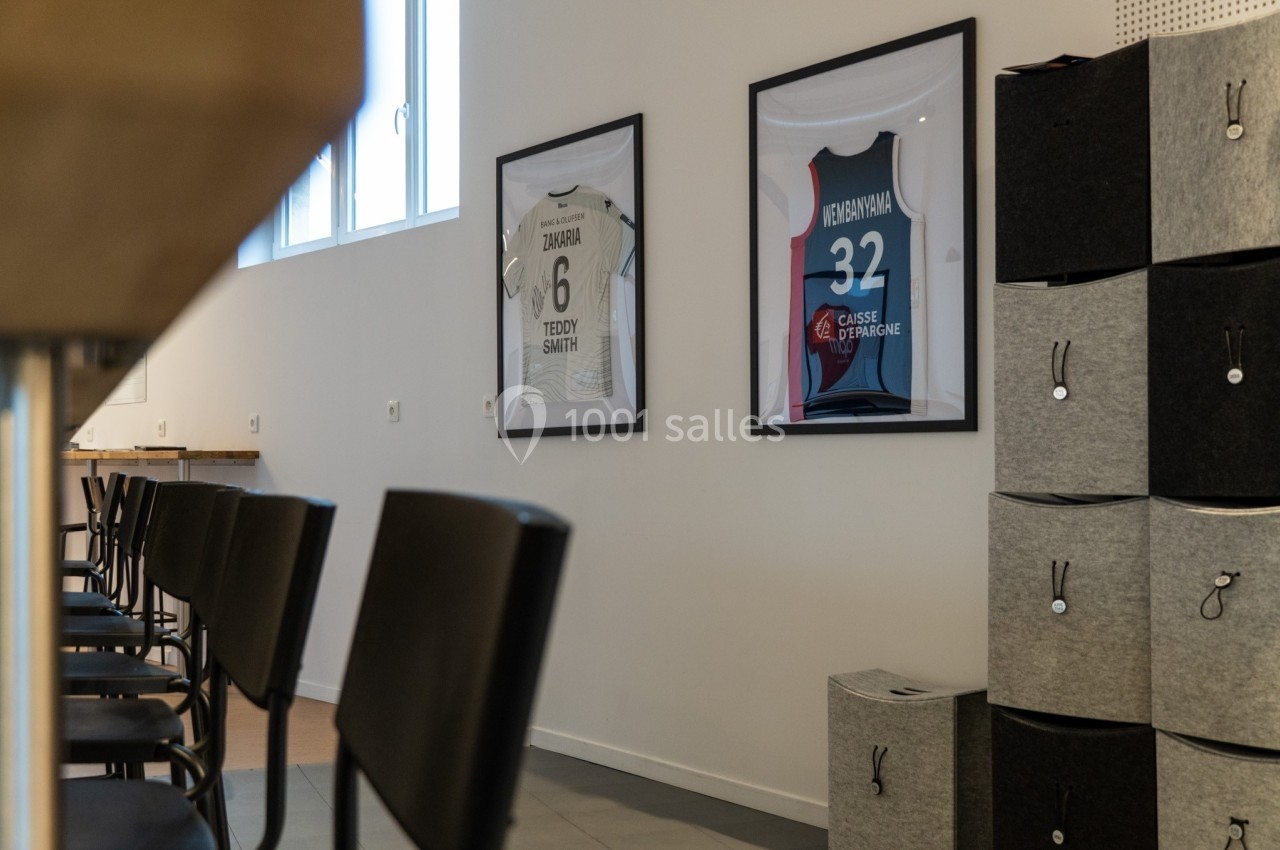 Deux cadres avec des maillots sportifs accrochés au mur dans une pièce avec des chaises et des rangements.