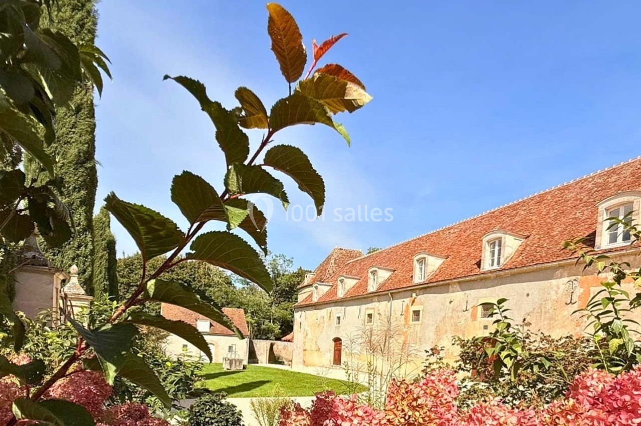 Bâtiments en pierre aux toits rouges entourés de végétation, avec des hortensias roses au premier plan.