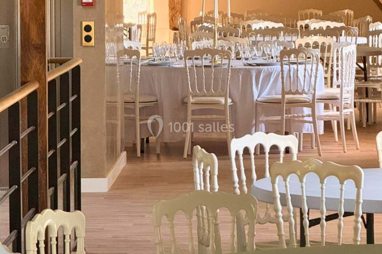 Salle de réception lumineuse avec tables rondes et chaises blanches, décorée pour un événement.