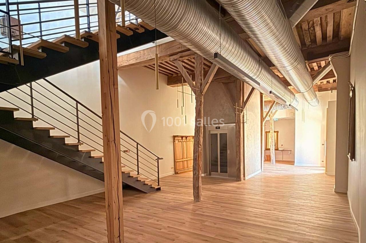 Intérieur spacieux avec parquet clair, poutres apparentes, escalier métallique et conduits de ventilation visibles.