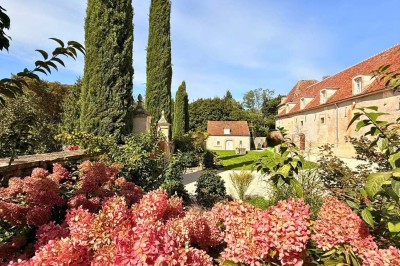 Miniature Location salle Magny (Yonne) - Château de Marrault #4 Jardin ensoleillé avec pelouse, puits en pierre, cyprès et bâtiment en pierre sous un ciel bleu dégagé.
