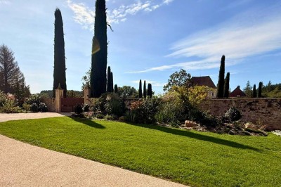 Miniature Location salle Magny (Yonne) - Château de Marrault #7 Jardin ensoleillé avec pelouse, puits en pierre, cyprès et bâtiment en pierre sous un ciel bleu dégagé.