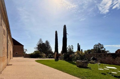 Miniature Location salle Magny (Yonne) - Château de Marrault #8 Jardin ensoleillé avec pelouse, puits en pierre, cyprès et bâtiment en pierre sous un ciel bleu dégagé.