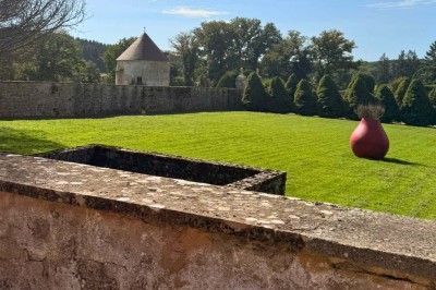Miniature Location salle Magny (Yonne) - Château de Marrault #10 Jardin ensoleillé avec pelouse, puits en pierre, cyprès et bâtiment en pierre sous un ciel bleu dégagé.
