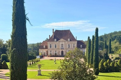 Miniature Location salle Magny (Yonne) - Château de Marrault #12 Jardin ensoleillé avec pelouse, puits en pierre, cyprès et bâtiment en pierre sous un ciel bleu dégagé.