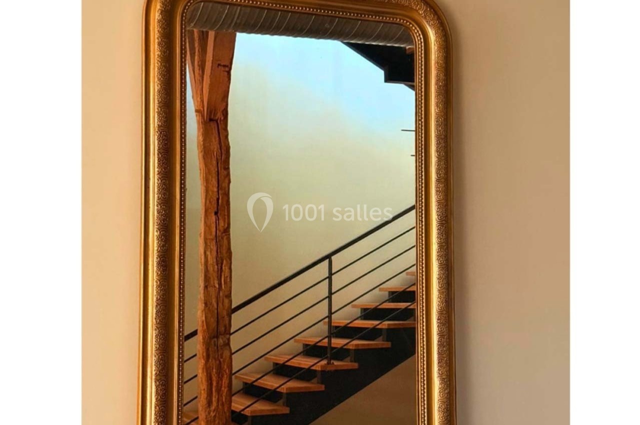 Miroir doré avec cadre orné, reflétant un escalier en bois et métal dans un intérieur lumineux.