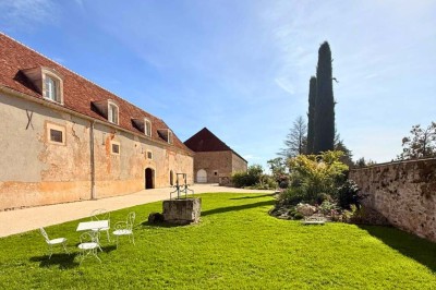 Miniature Location salle Magny (Yonne) - Château de Marrault #23 Jardin ensoleillé avec pelouse, puits en pierre, cyprès et bâtiment en pierre sous un ciel bleu dégagé.