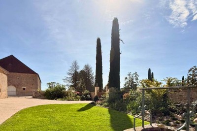 Miniature Location salle Magny (Yonne) - Château de Marrault #24 Jardin ensoleillé avec pelouse, puits en pierre, cyprès et bâtiment en pierre sous un ciel bleu dégagé.