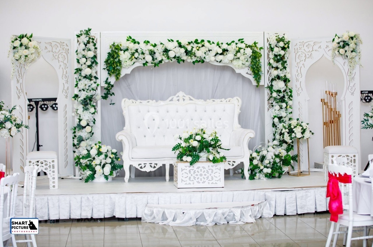 Décor de mariage avec canapé blanc, table assortie et fleurs blanches et vertes sur une estrade ornée.