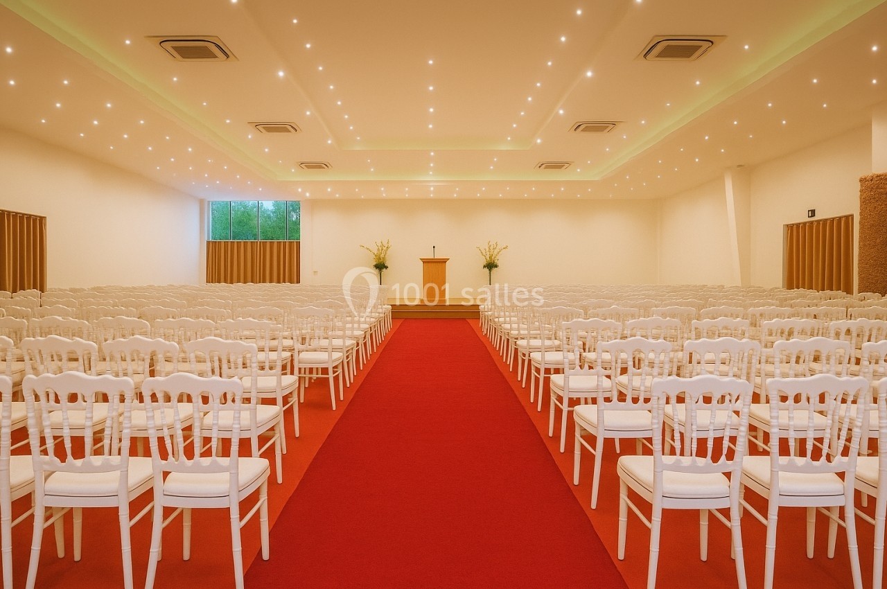 Salle de conférence lumineuse avec rangées de chaises blanches alignées et un pupitre sur une estrade au fond.