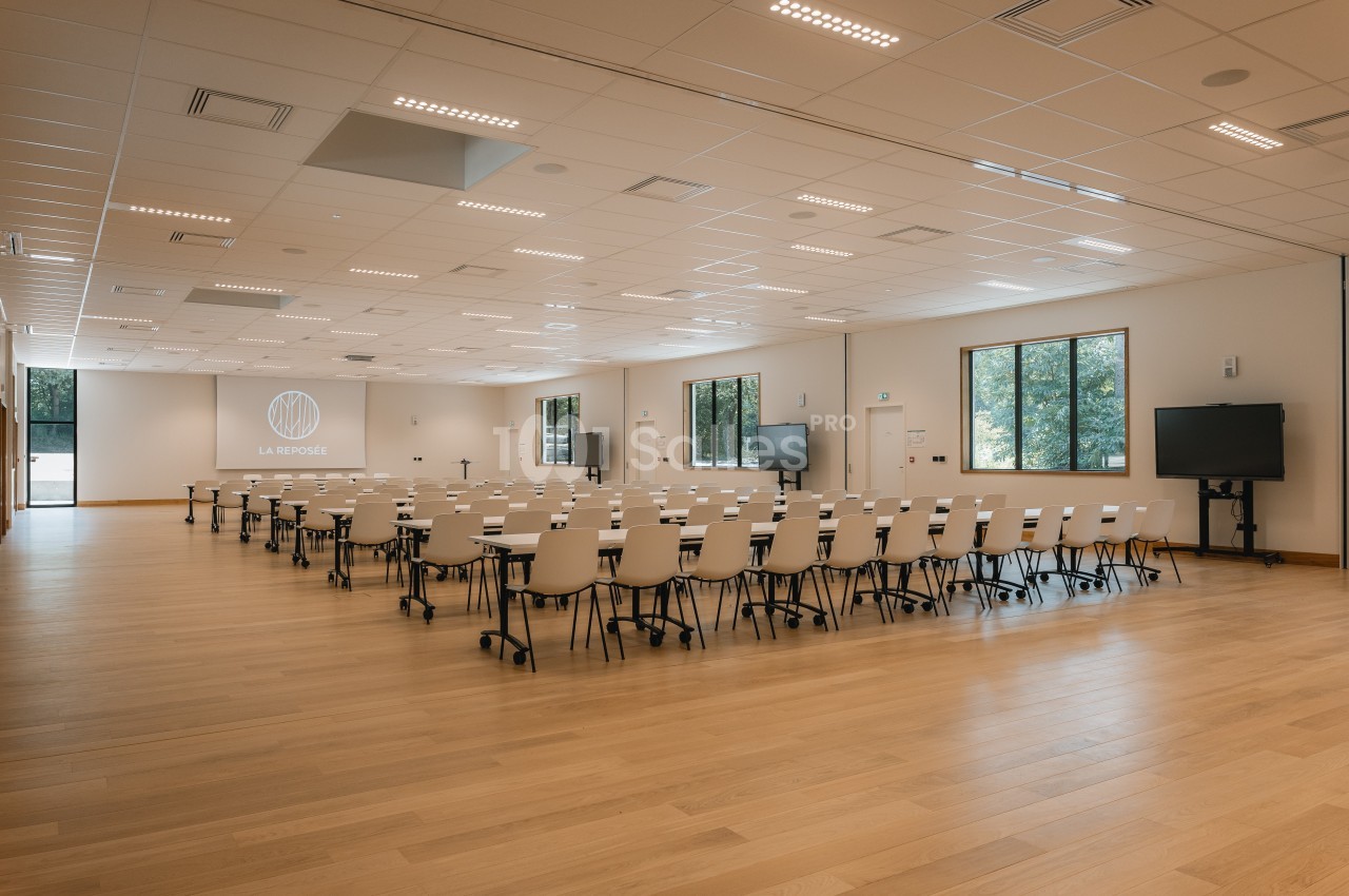 Salle de conférence lumineuse avec des rangées de chaises blanches, des écrans et un projecteur allumé.