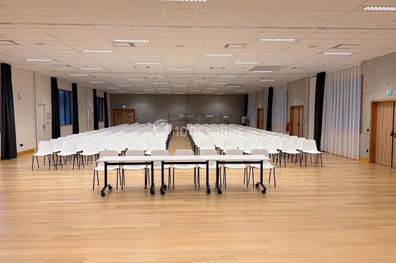 Salle de conférence vide avec des rangées de chaises blanches alignées et des tables à l'avant, éclairée par des lumières au…