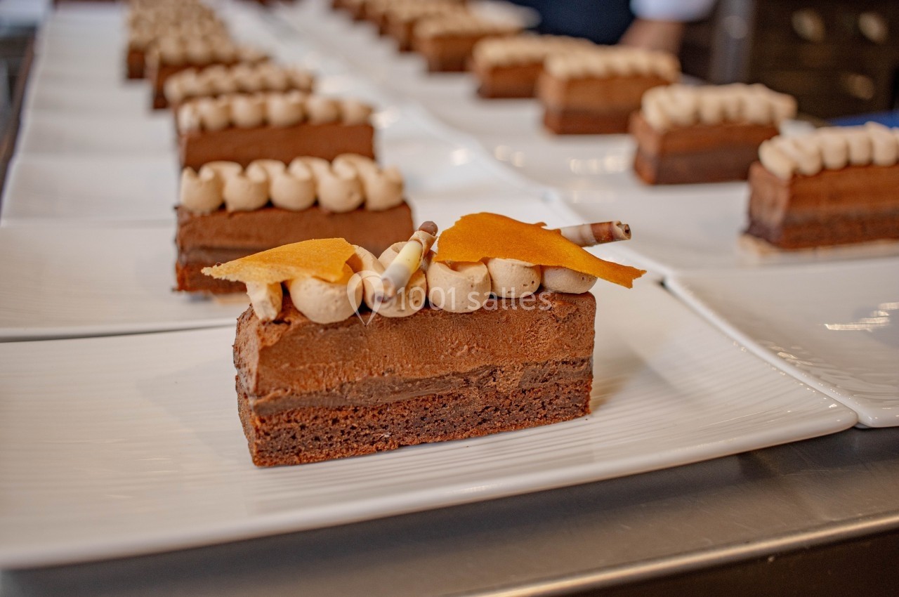 Part de gâteau au chocolat décorée de crème, de copeaux et de morceaux de caramel, présentée sur une assiette blanche.