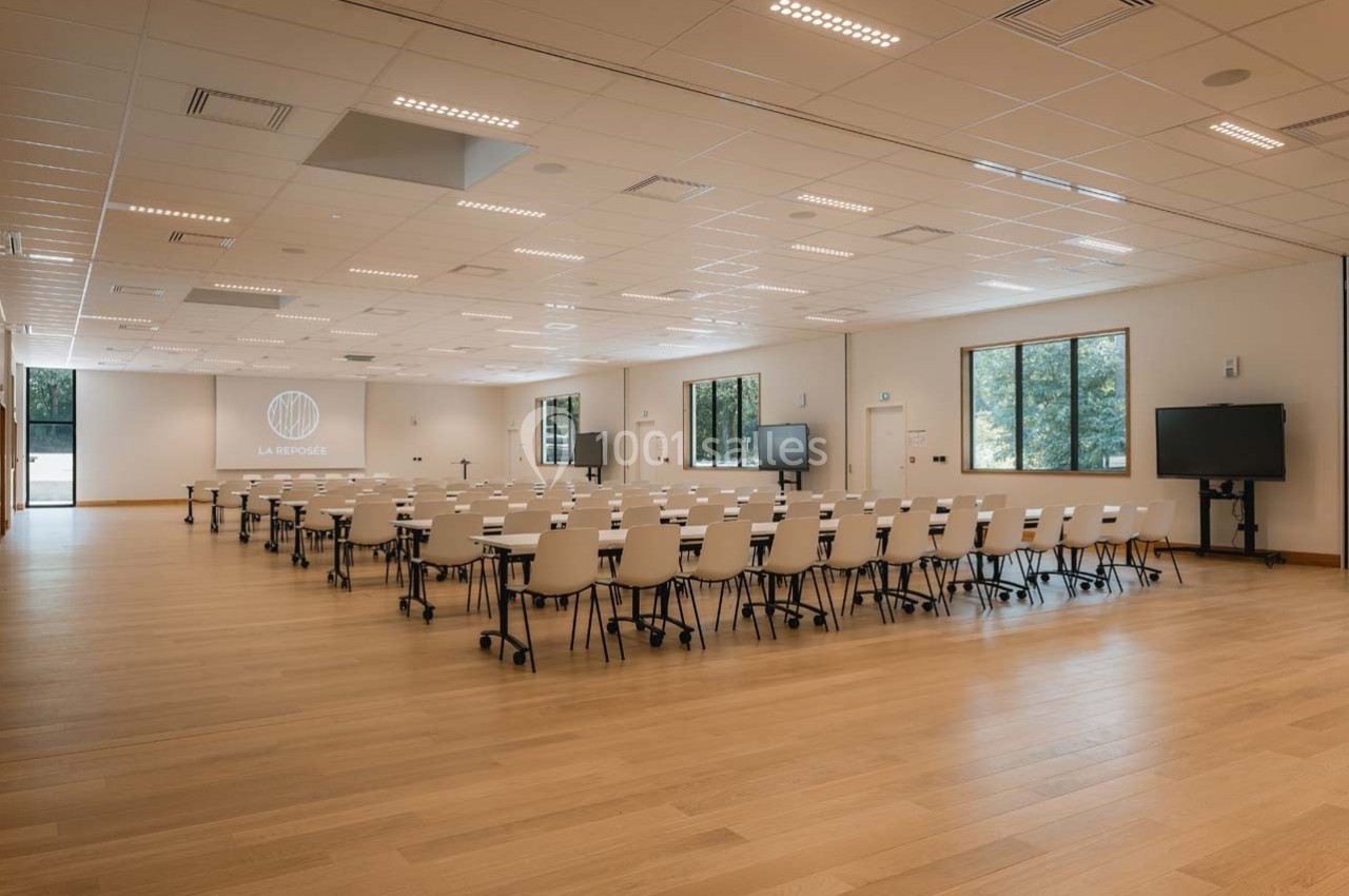 Salle de conférence lumineuse avec des rangées de chaises blanches, un écran de projection et des fenêtres donnant sur l…