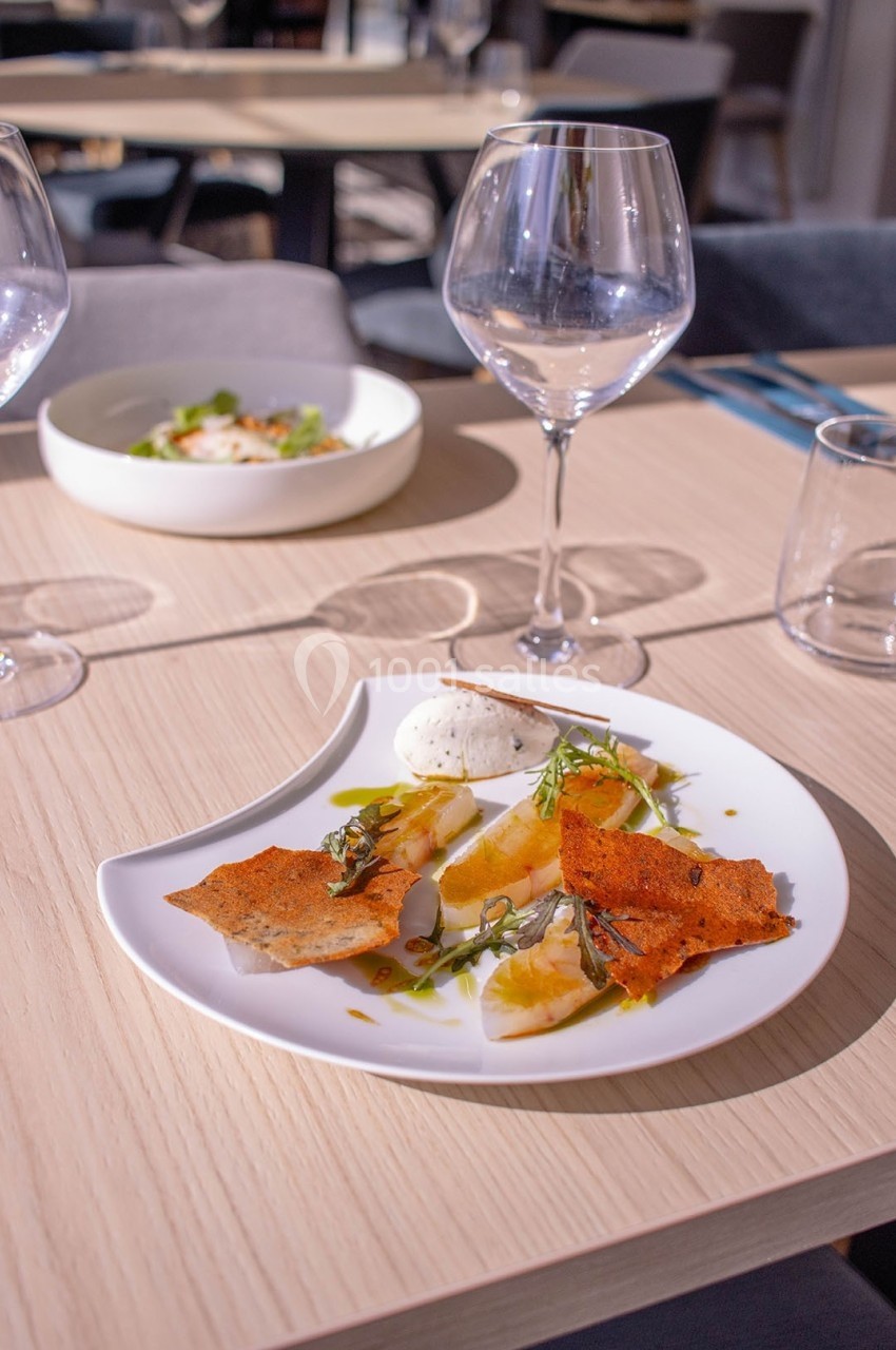 Assiette gastronomique avec poisson, chips croustillantes, herbes fraîches et crème, servie sur une table en bois clair.