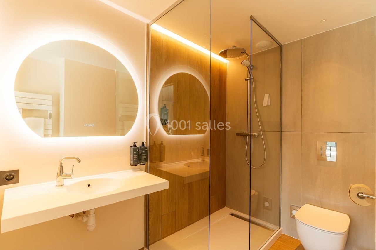 Salle de bain moderne avec douche à l'italienne, lavabo blanc, miroir rond éclairé et toilettes.