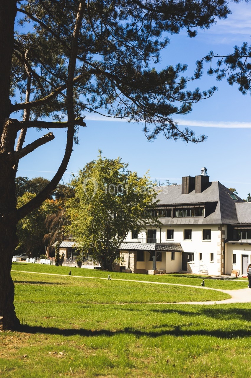 Bâtiment moderne entouré d'arbres et d'une pelouse verte sous un ciel bleu clair.