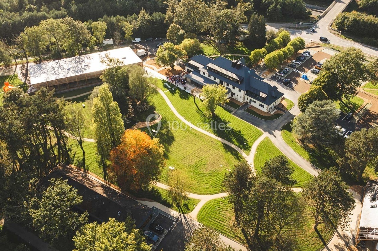 Vue aérienne d'un complexe entouré d'arbres, comprenant plusieurs bâtiments, des parkings et des espaces verts aménagés.