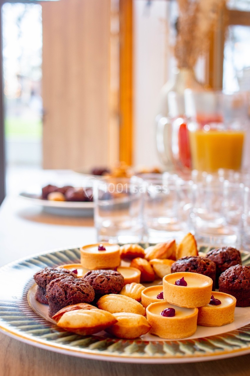 Assortiment de pâtisseries sur une assiette, avec un pichet de jus d'orange et des verres en arrière-plan.