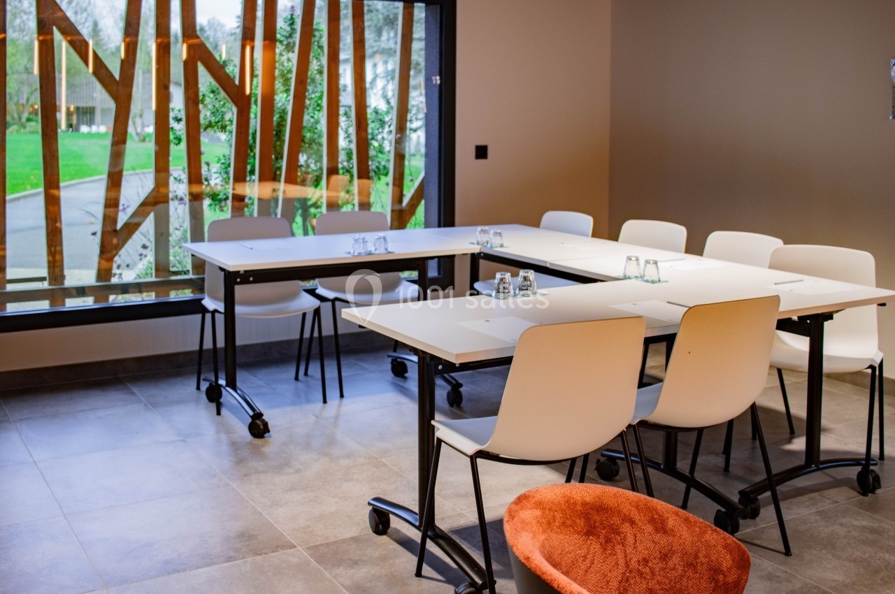 Salle de réunion lumineuse avec des tables modulables, des chaises blanches et une grande baie vitrée donnant sur un jardin.