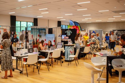 Salle d'exposition avec stands d'information, visiteurs échangeant et explorant divers produits et services.