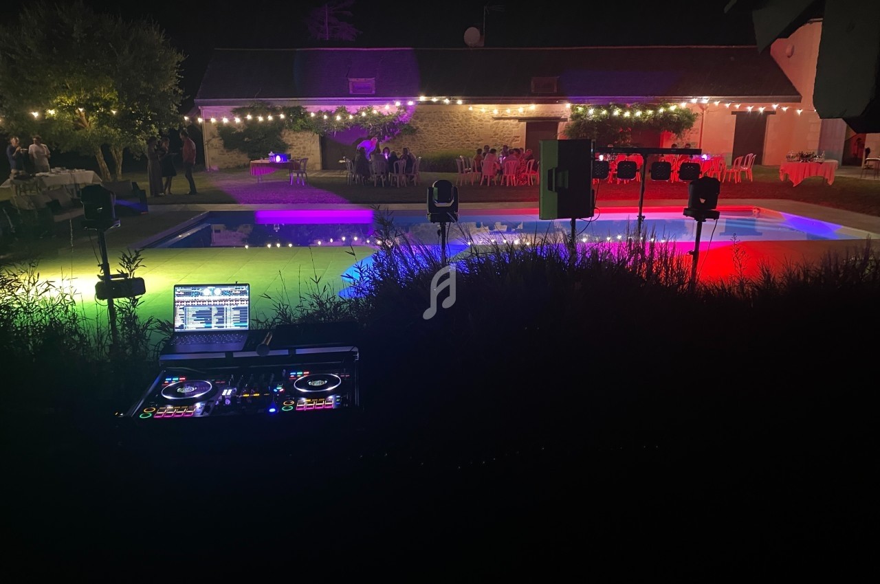 Vue nocturne d'une piscine éclairée par des lumières colorées, avec une table de mixage en premier plan.