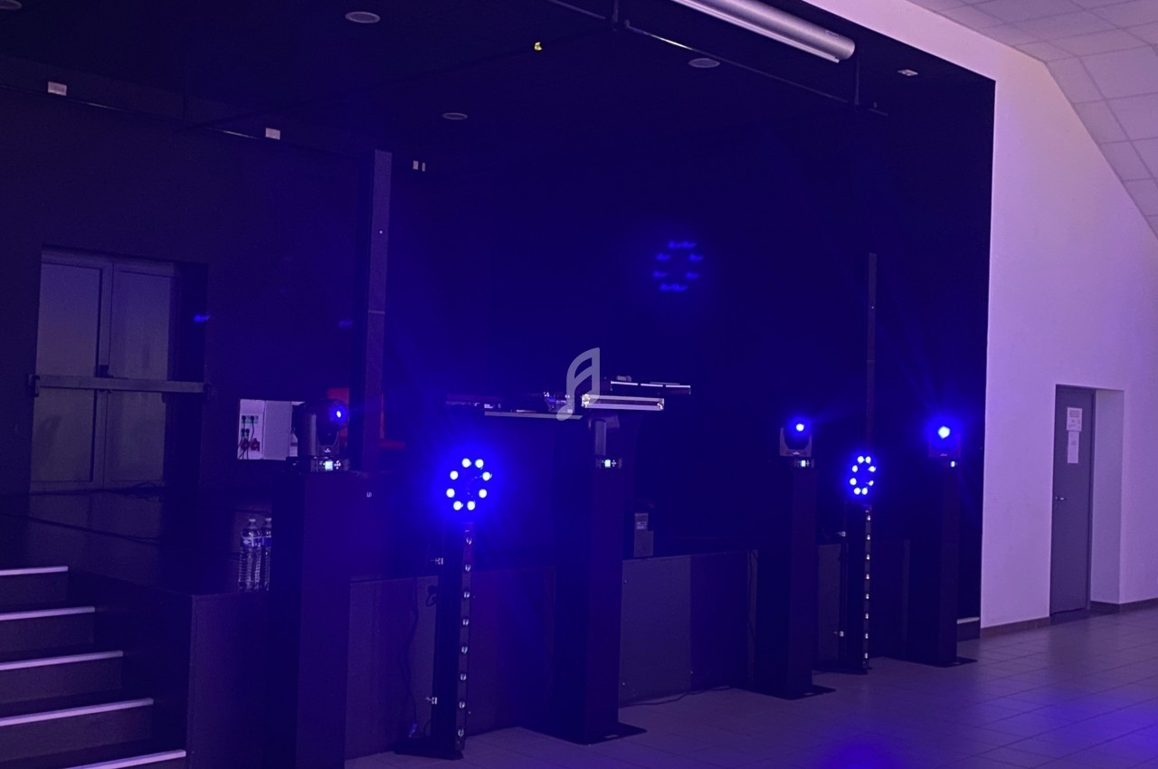 Scène intérieure sombre avec projecteurs LED bleus allumés et équipement audio visible.