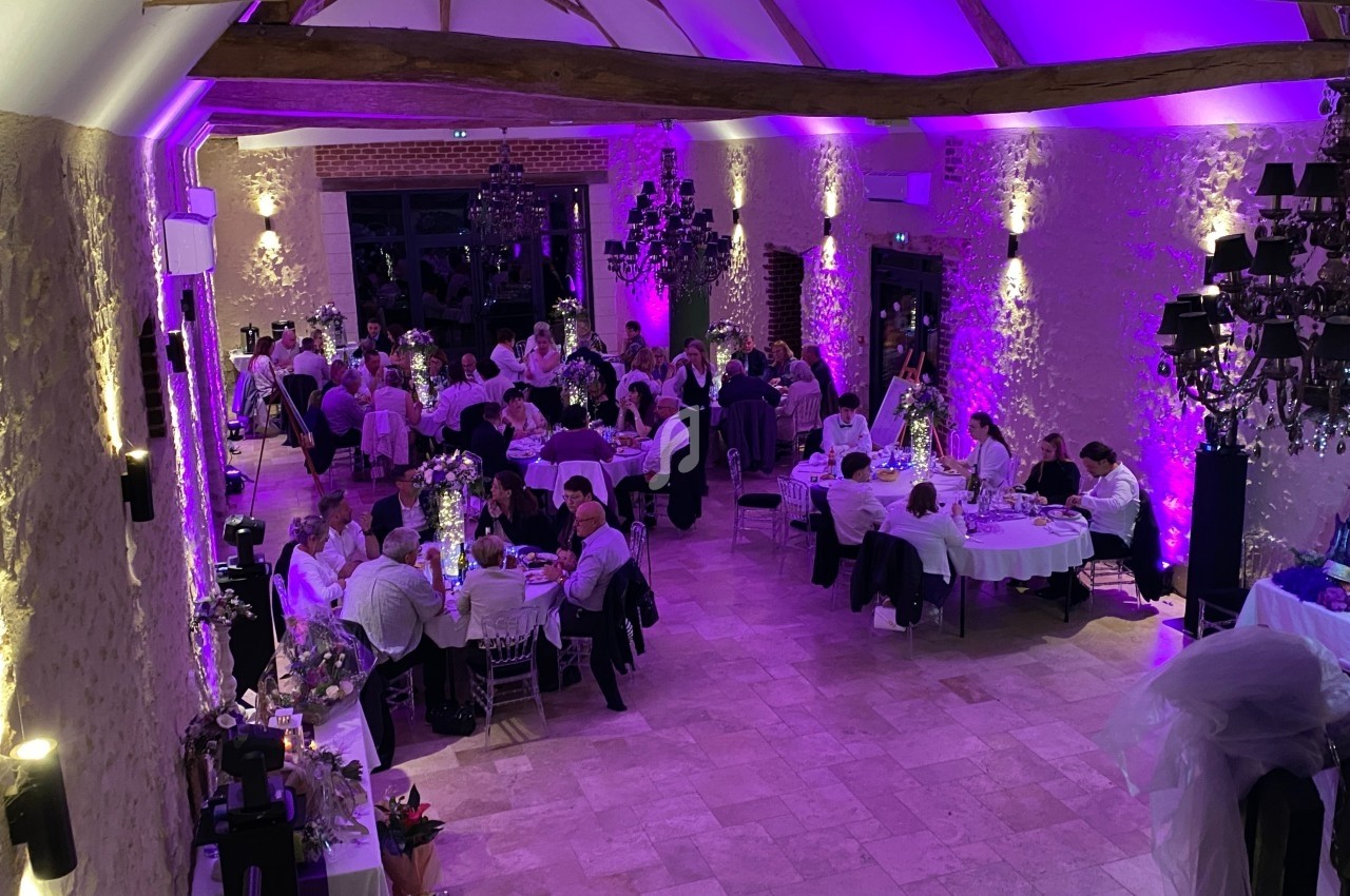 Salle de réception décorée avec des lumières violettes, des invités assis à des tables rondes lors d'un événement.