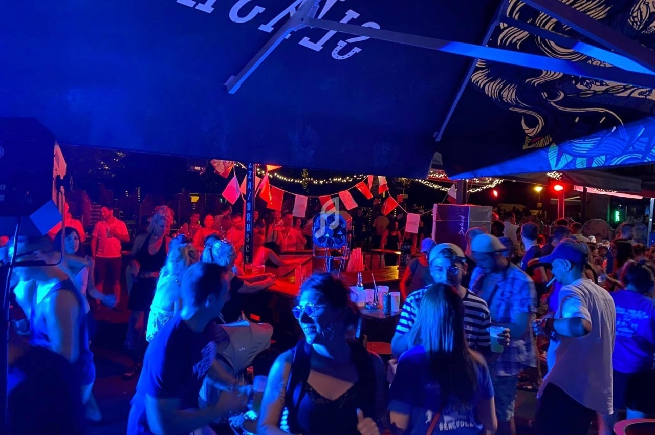 Groupe de personnes dansant et socialisant sous des lumières colorées dans un espace extérieur animé.
