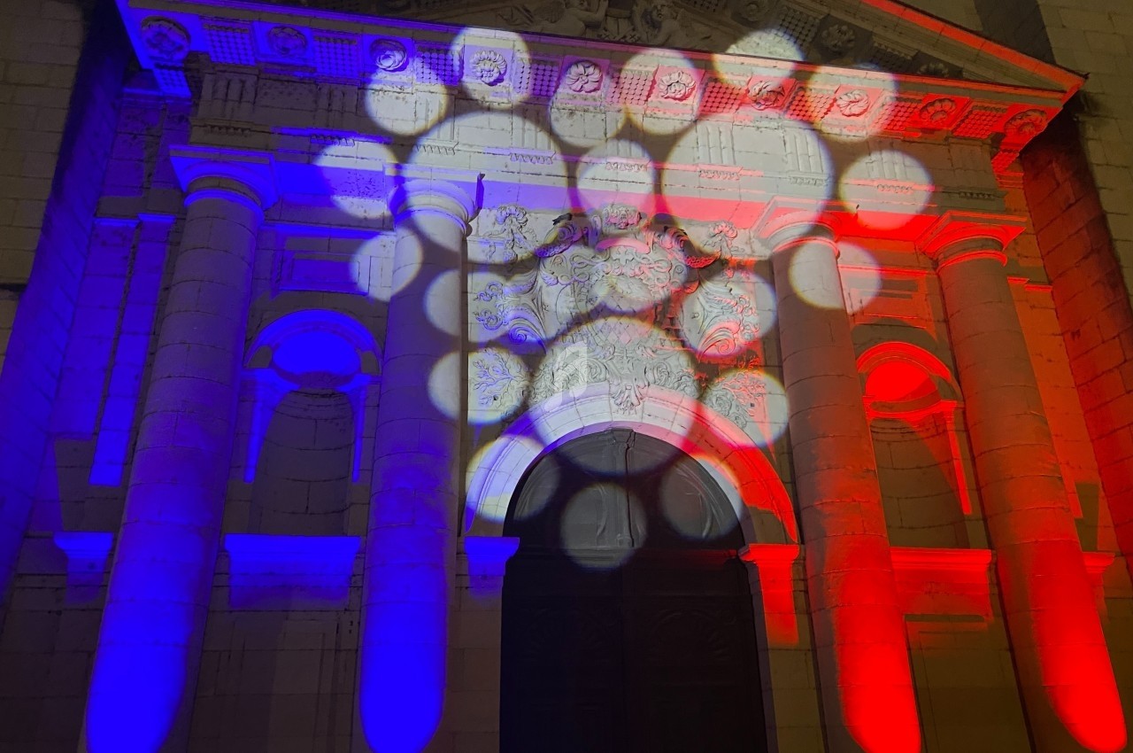 Façade d'un bâtiment illuminée par des projections de lumière aux couleurs bleu, blanc et rouge.