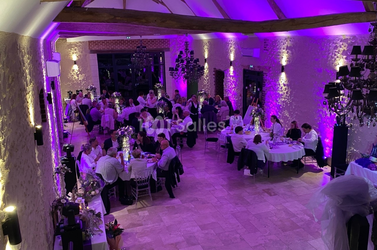 Salle de réception avec des invités assis à des tables rondes, éclairée par une lumière violette et des lustres noirs.