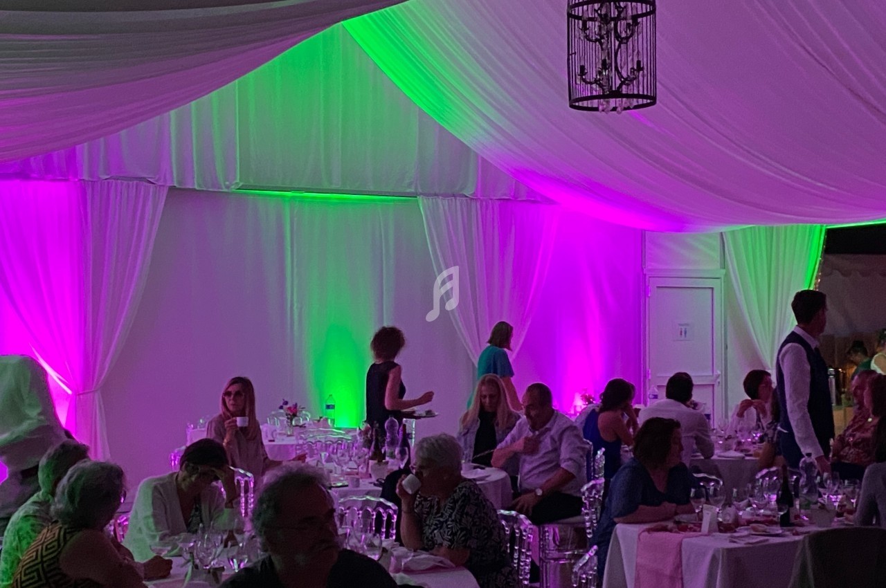 Salle de réception avec des invités dînant sous une tente éclairée par des lumières violettes et vertes.