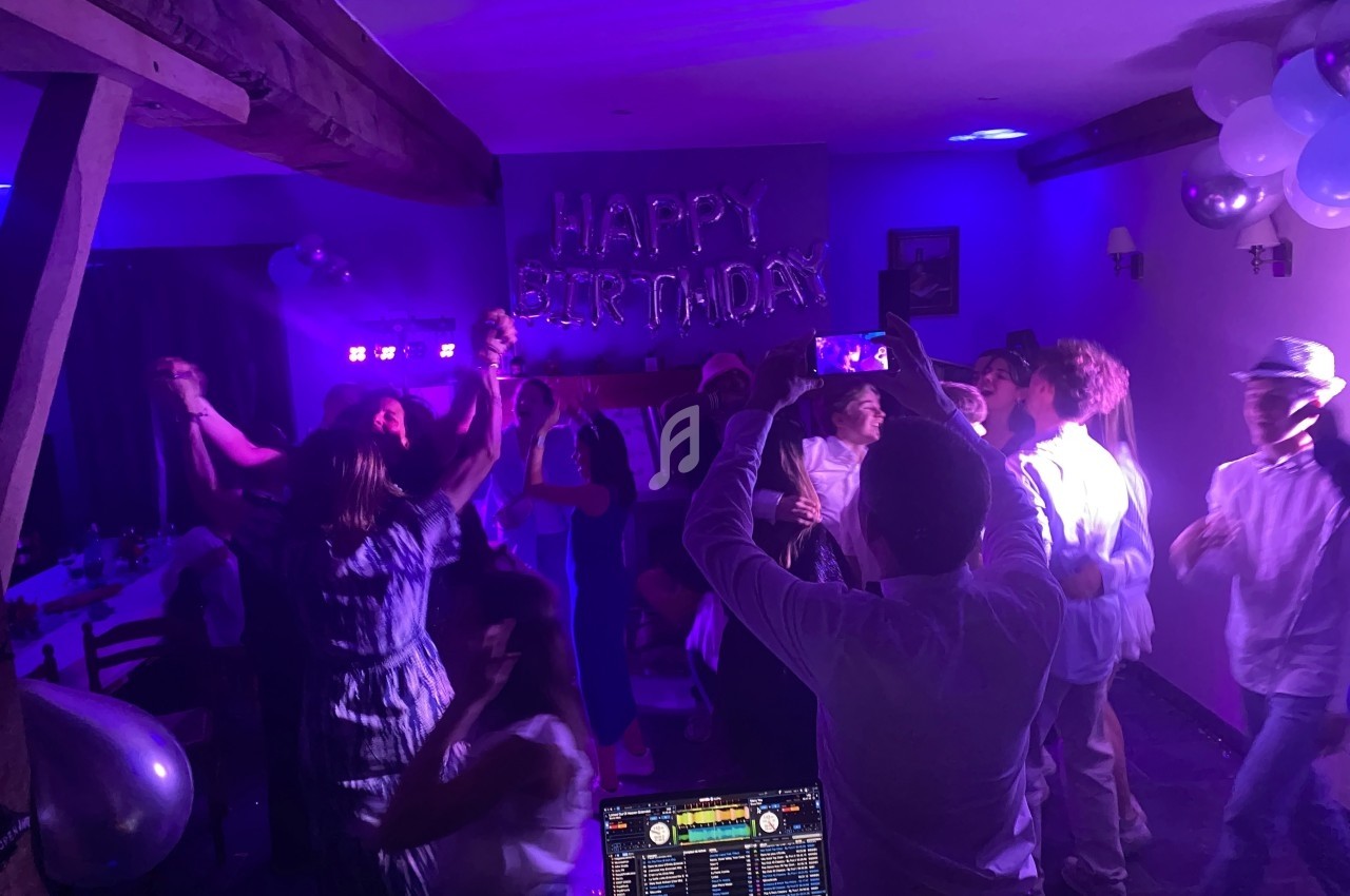 Personnes dansant et célébrant un anniversaire dans une salle décorée avec des lumières colorées et des ballons.