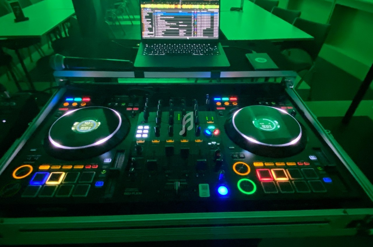 Table de mixage DJ éclairée avec des boutons colorés, accompagnée d'un ordinateur portable affichant une interface musicale.