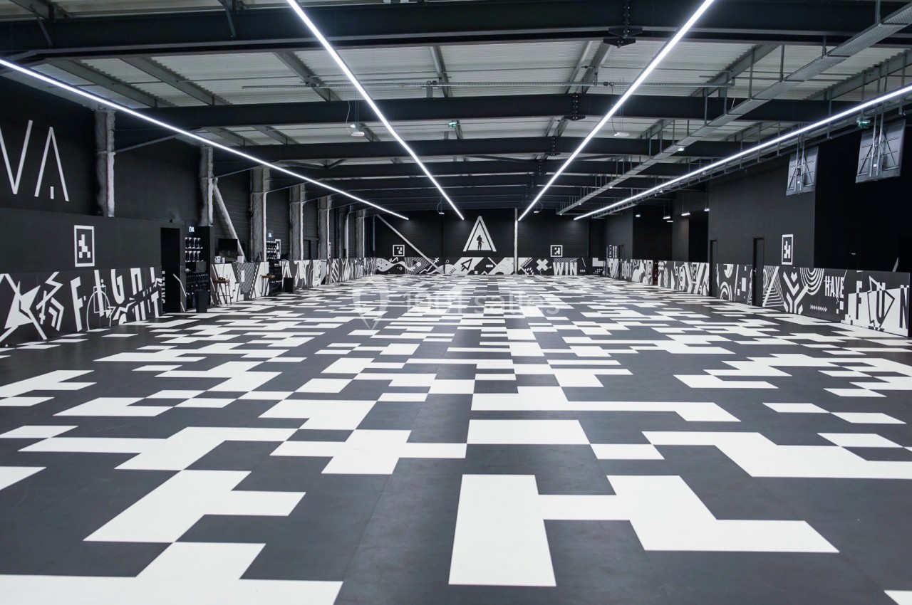 Salle intérieure avec un sol en damier noir et blanc, entourée de murs sombres décorés de motifs géométriques.