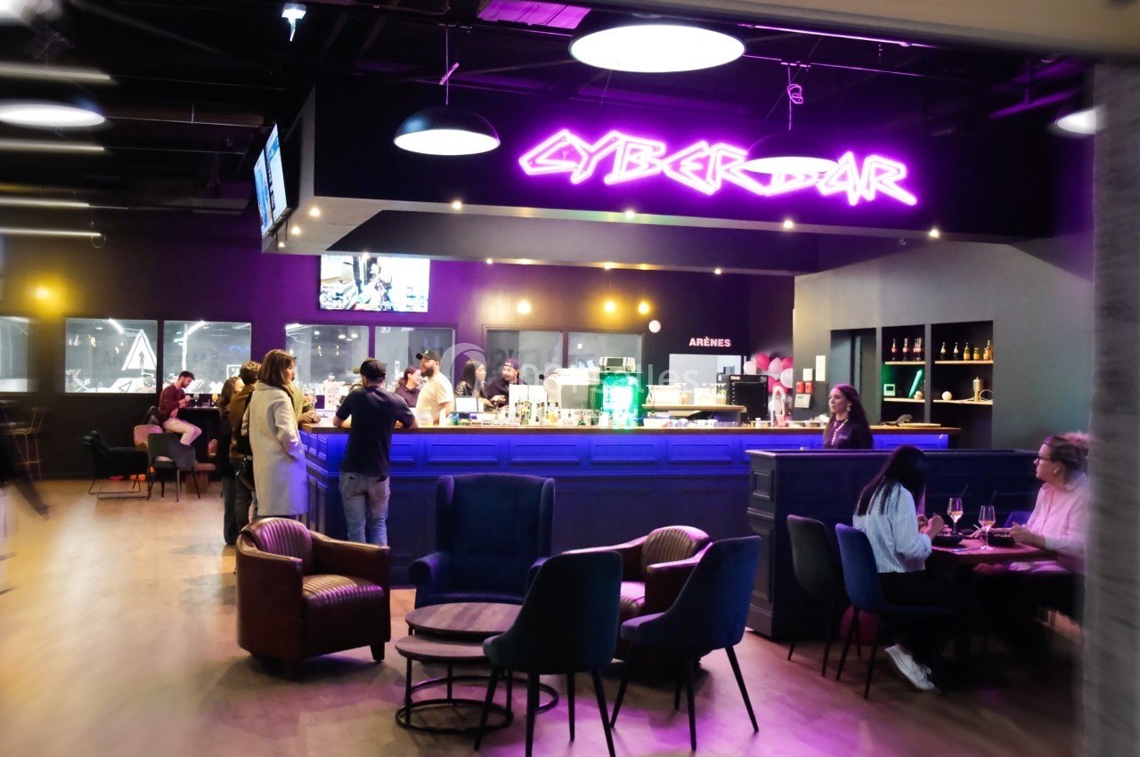 Intérieur d'un bar moderne avec un éclairage néon violet, des clients assis et un comptoir central animé.