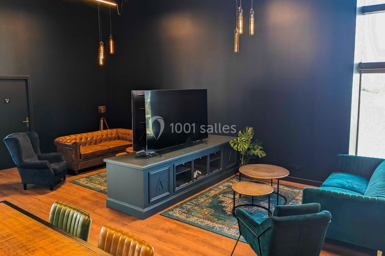 Salon moderne avec canapé en cuir, fauteuils, tapis coloré, meuble TV et éclairage suspendu dans une pièce sombre.