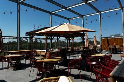 Espace extérieur avec canapés, parasols et écran géant, entouré de structures métalliques et de bois.