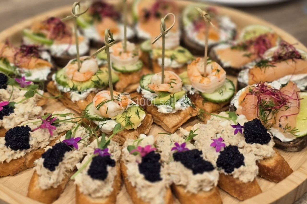 Plateau de toasts variés garnis de crevettes, caviar, herbes fraîches et fleurs comestibles, présenté sur une table en bois.