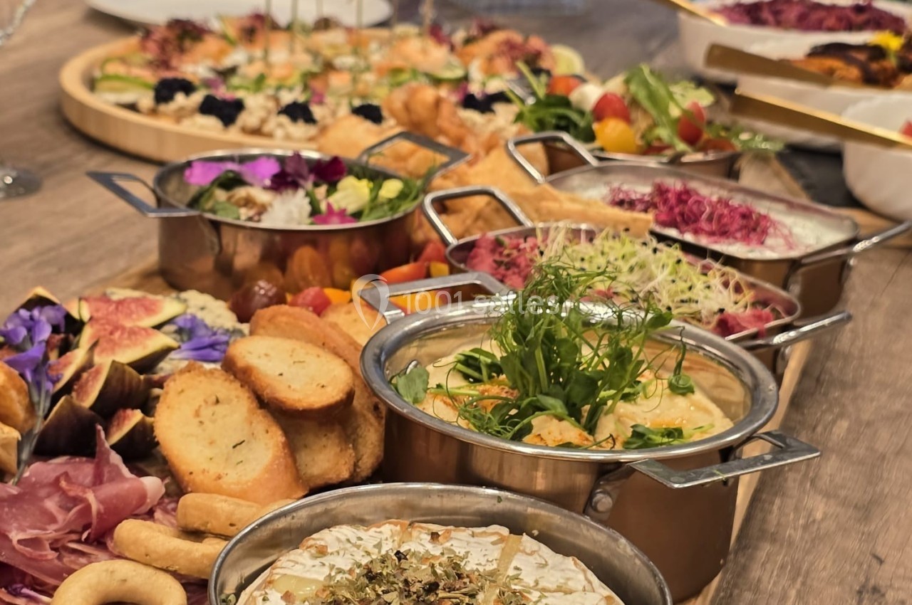 Table garnie de plats variés, incluant fromages, charcuteries, salades et tartinades, présentés dans des récipients élégants.
