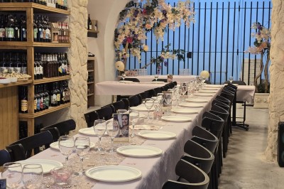 Table et deux chaises noires installées devant un mur beige avec une enseigne ’Nevian's Traiteur & Cave’.