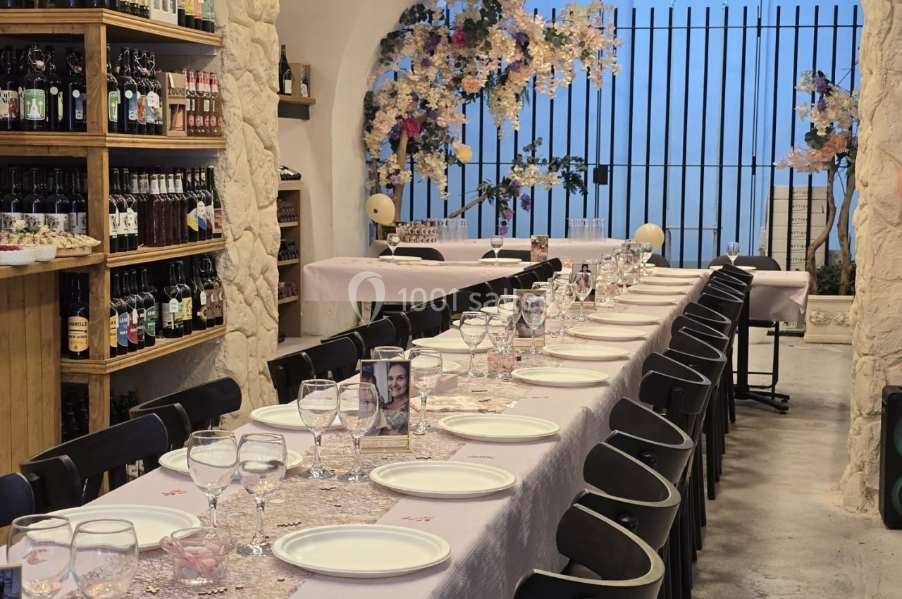 Table dressée pour un repas festif dans une salle voûtée avec étagères de bouteilles et décoration florale.
