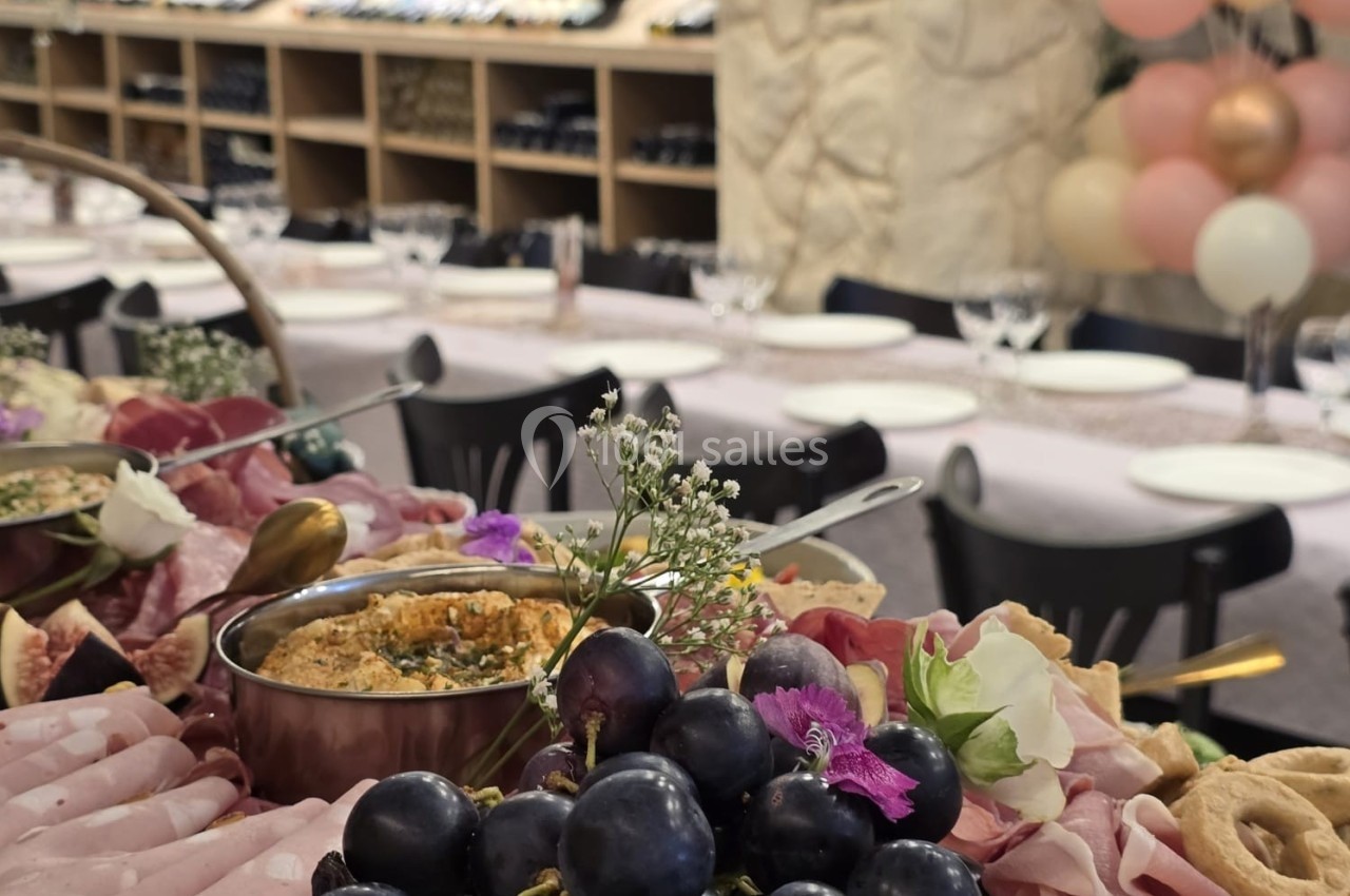 Plateau de charcuterie, raisins et dips en gros plan, avec une table dressée et des étagères de bouteilles en arrière-plan.